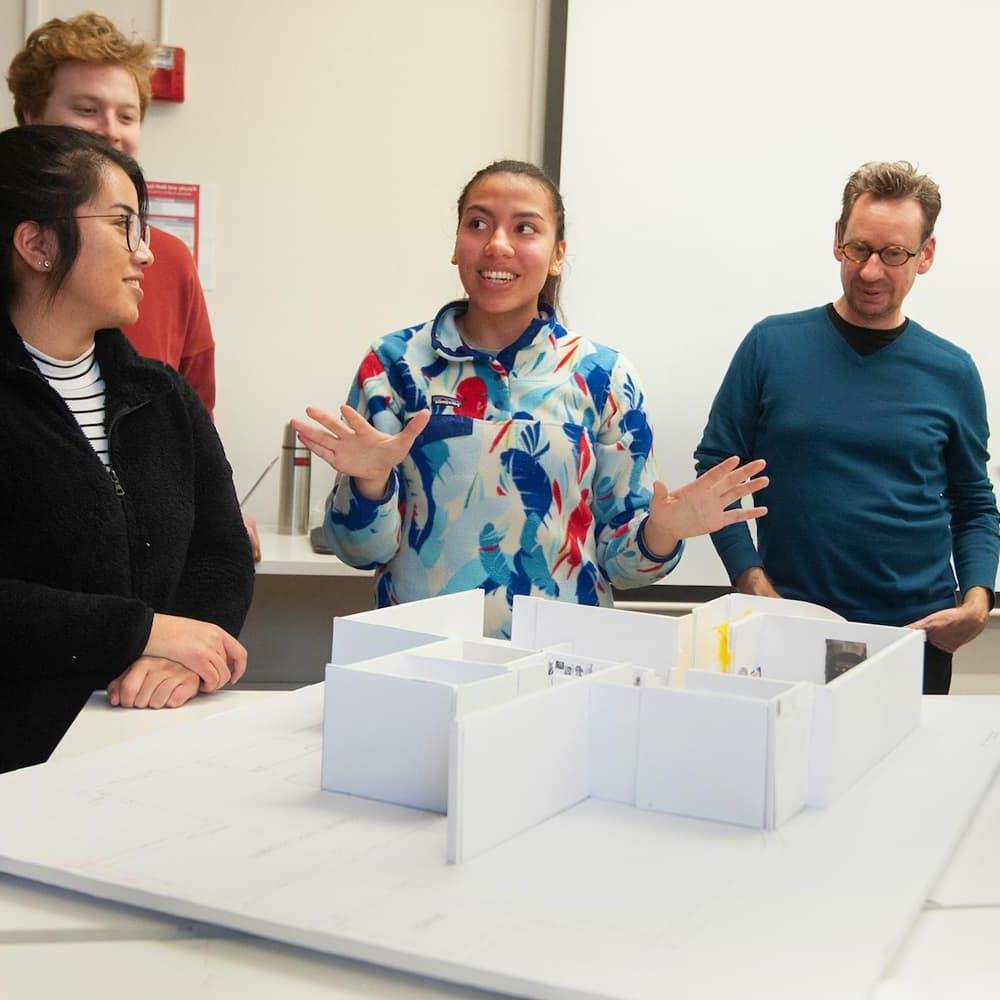 在设计课上，三个学生和一个教授在看一个建筑模型.